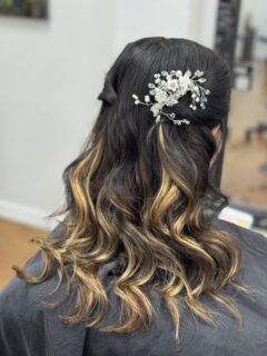 Half-up dark hairstyle with blonde highlights, curls and a floral hair accessory.