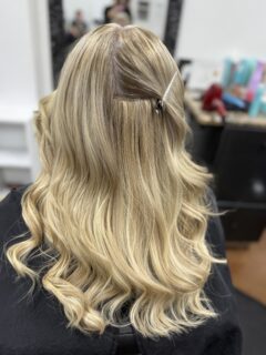 Half-up blonde hairstyle with loose curls and a small hair clip.